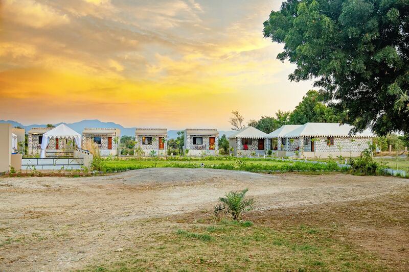 Jawai Heaven at sunset: tents and stone cottages on the lawn, with the Aravalli hills behind